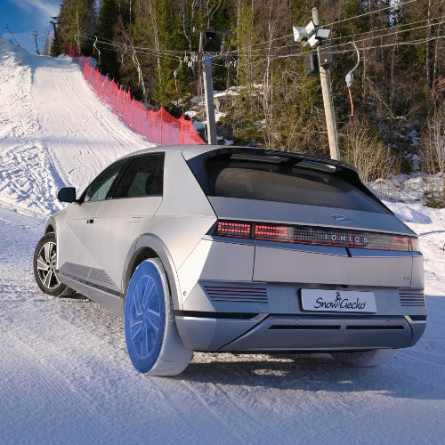A passenger car with SnowGecko mounted on rear wheels, standing on hill in ski area