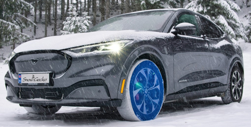 SnowGecko mounted on front wheels of a passenger car, standing on snow in nature